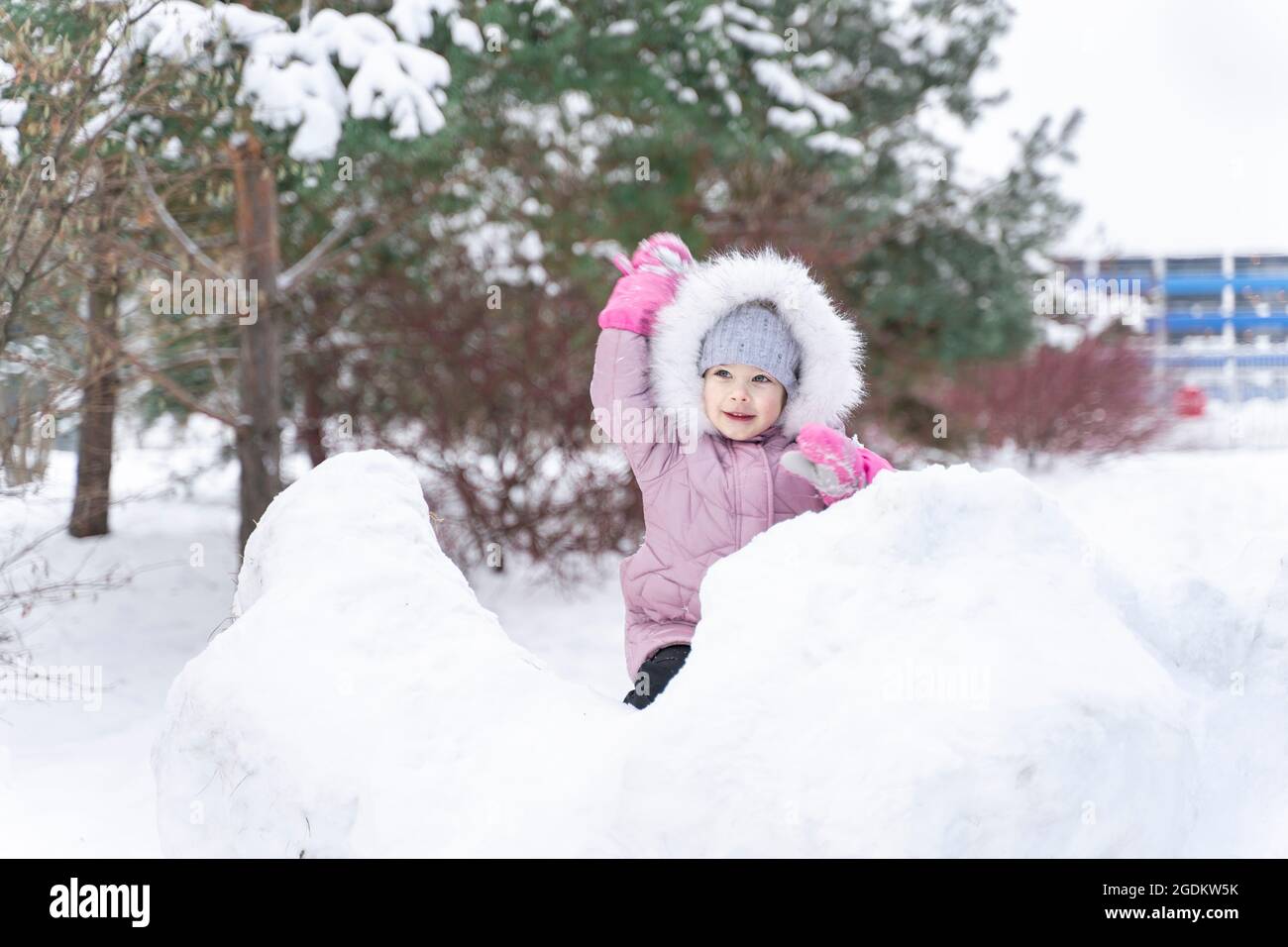 little girl in a warm coat and a hood plays snowballs in a snow ...