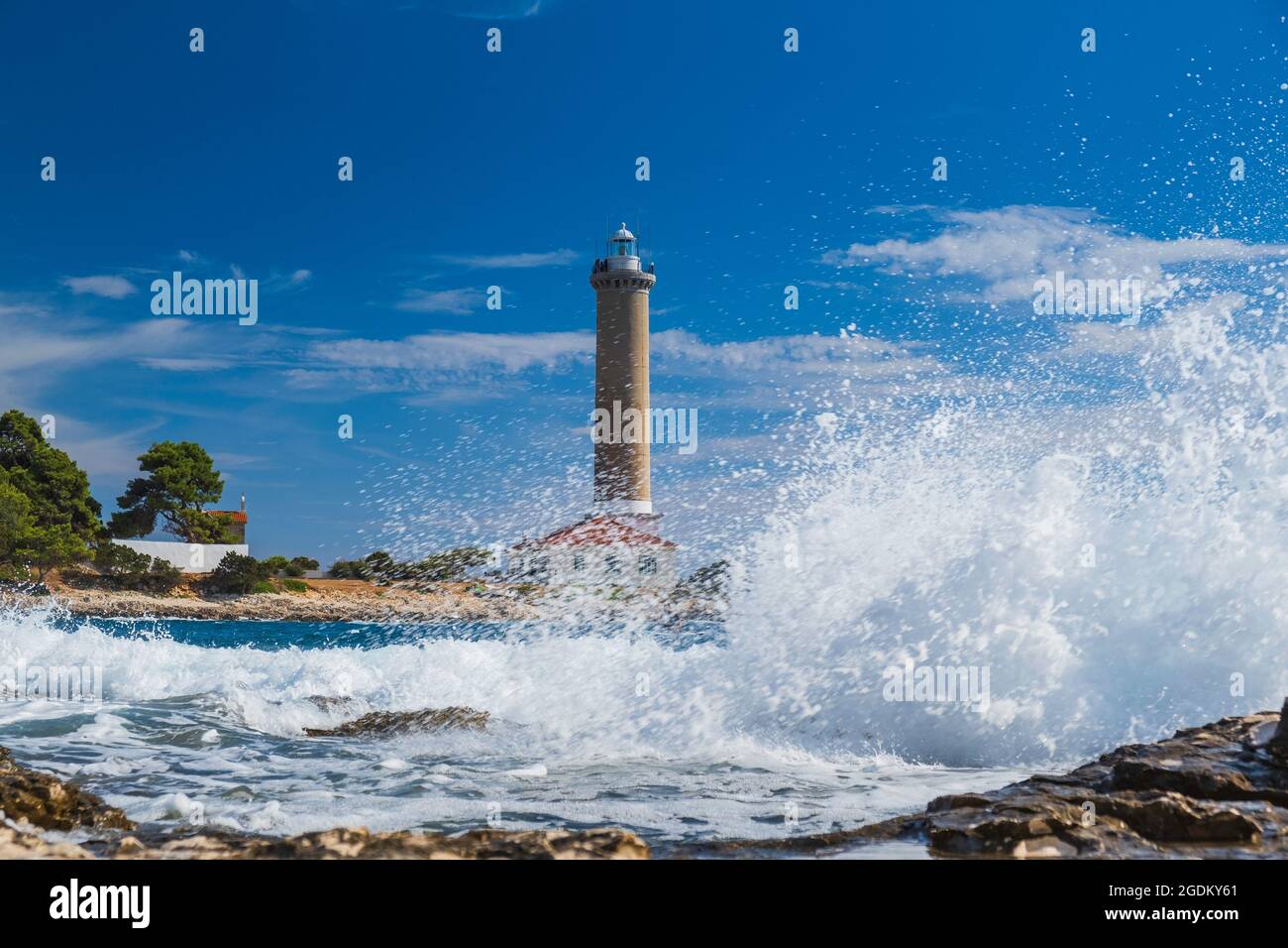 Sea waves breaking on rocks, lighthouse of Veli Rat on the island of Dugi Otok, Croatia in background Stock Photo