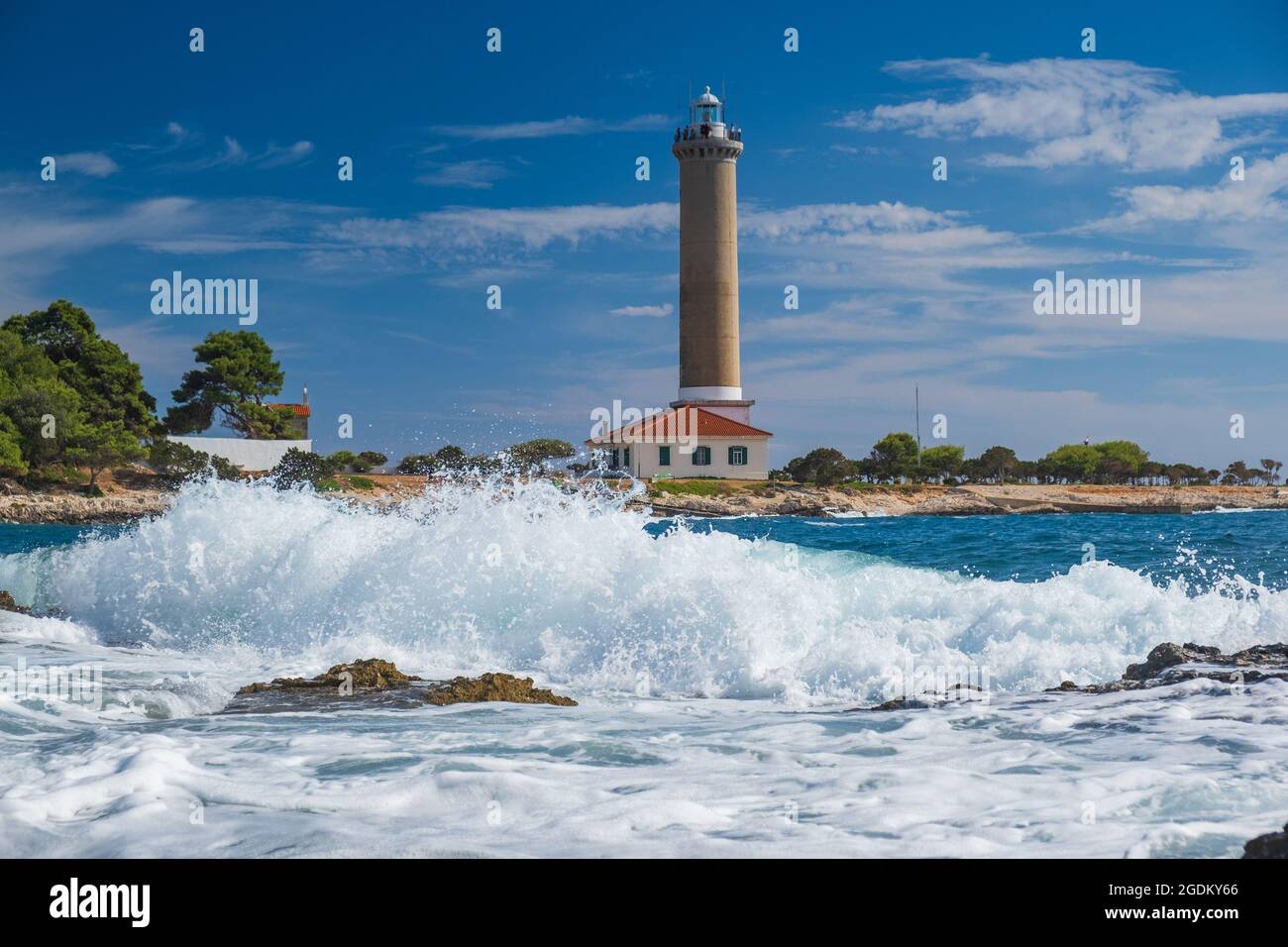 Sea waves breaking on rocks, lighthouse of Veli Rat on the island of Dugi Otok, Croatia in background Stock Photo