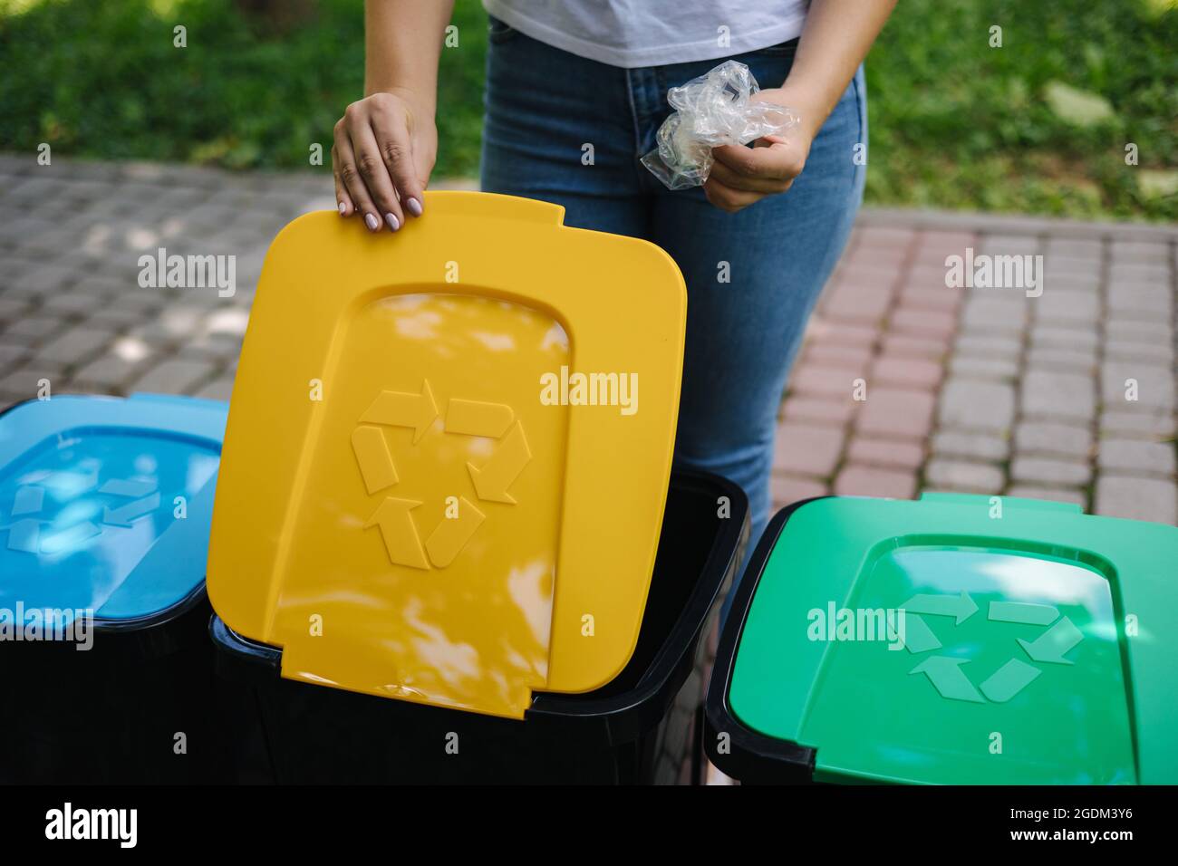 Female in the park throwing plastic bag into recycling bin. Different colours on plastic bins