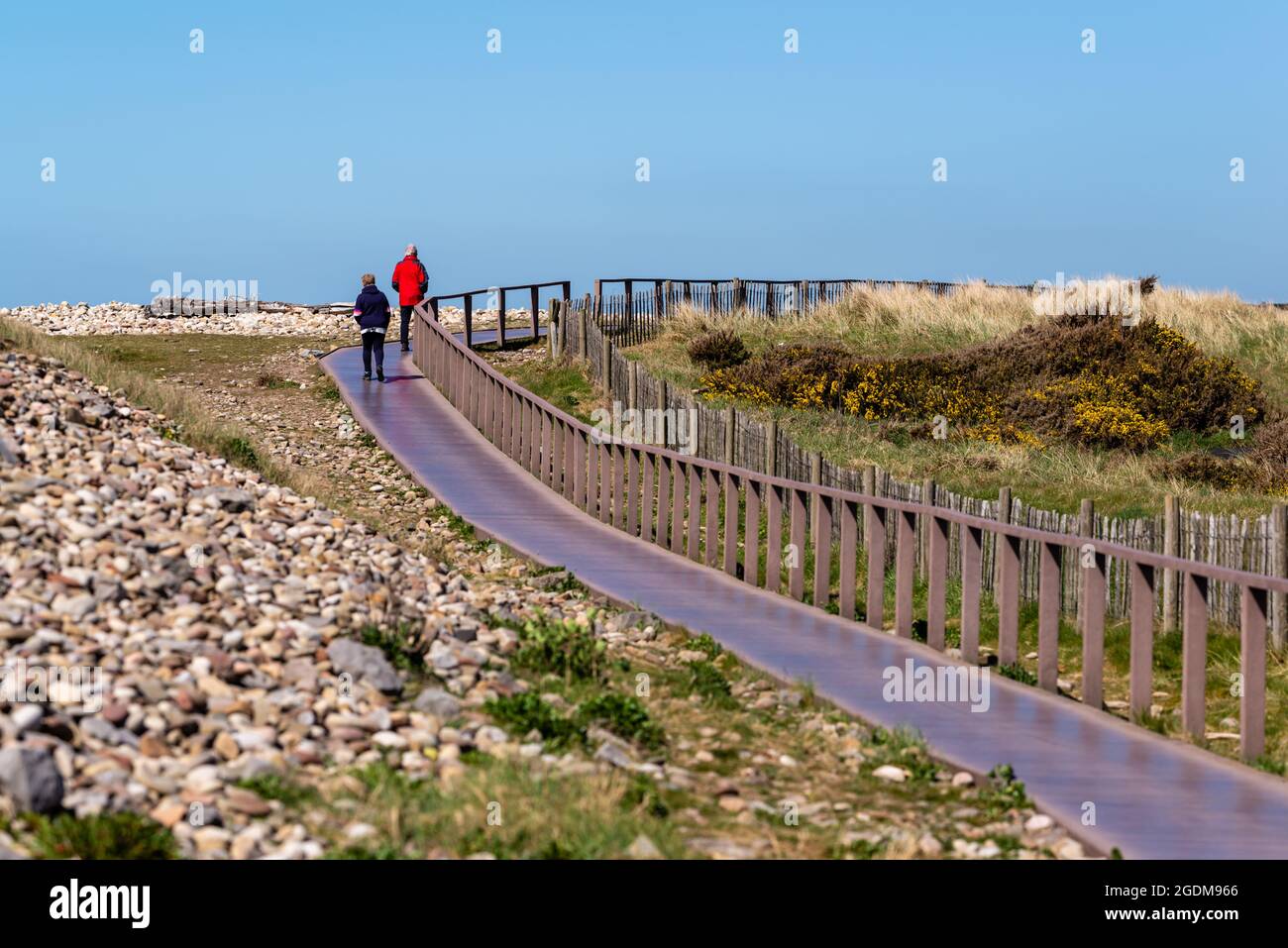 A couple walking along the broadwalk which forms part of the Wales Coastal Path Stock Photo