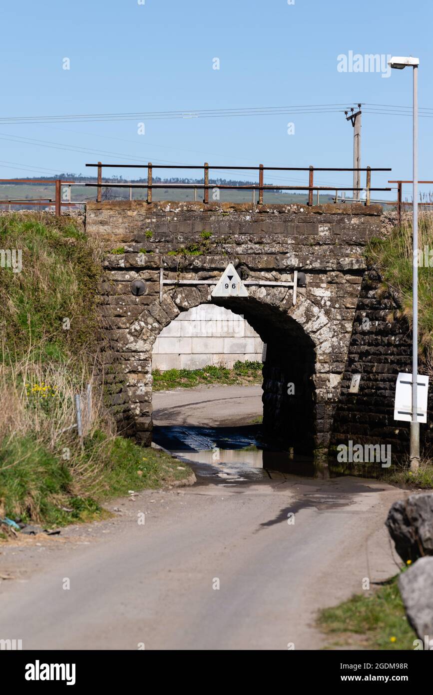 A height restricted railway bridge over a road for single file traffic Stock Photo