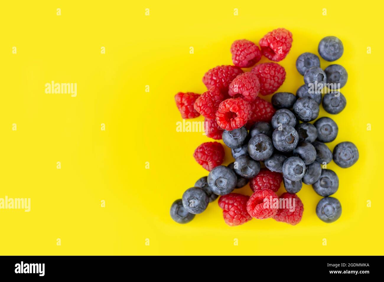 Delicious fresh organic blueberries and raspberries on bright yellow background with copy space. Stock Photo