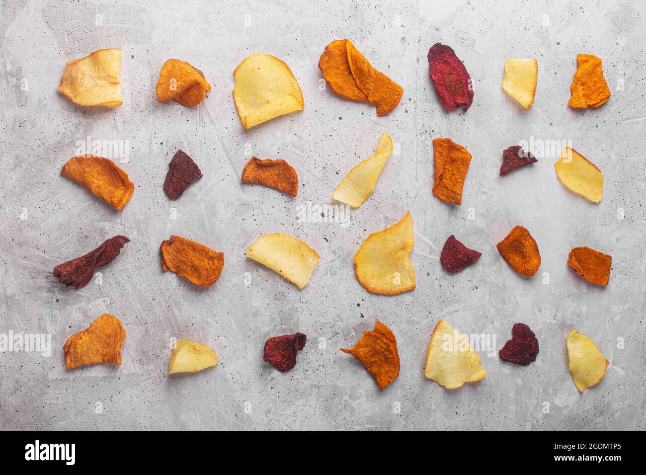 Layered rows of vegetable chips from potatoes, beets and carrots on a concrete background top view Stock Photo