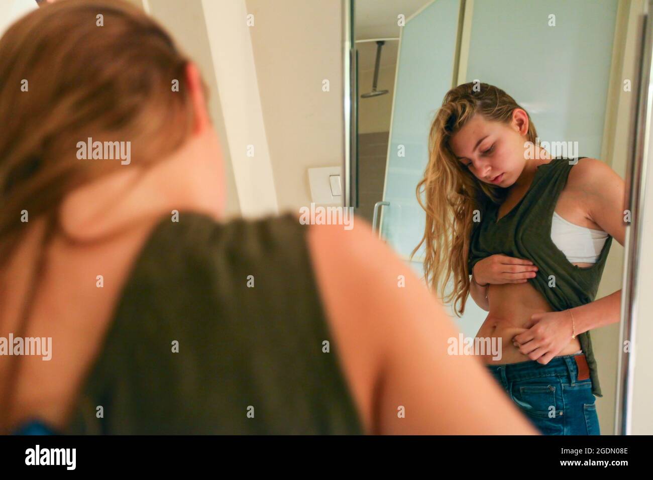 Young Woman pinching her waist. She may be keeping track of weight loss during a diet but compulsive body analysis may be a symptom of a body image di Stock Photo