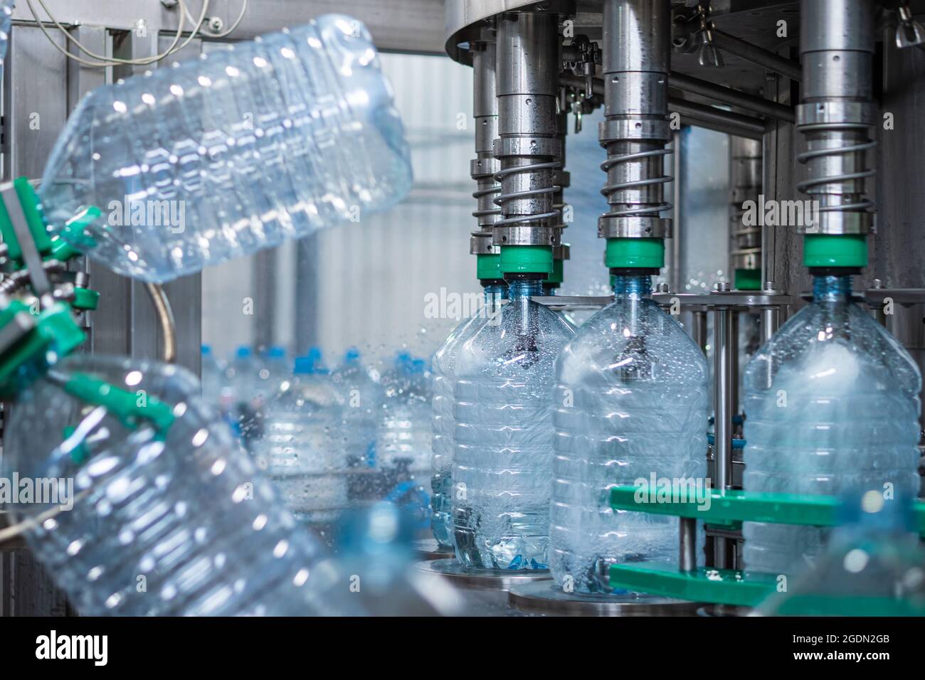Five-liter plastic bottles are filled with water in a filling machine. Automated production of drinking water. Food production Stock Photo