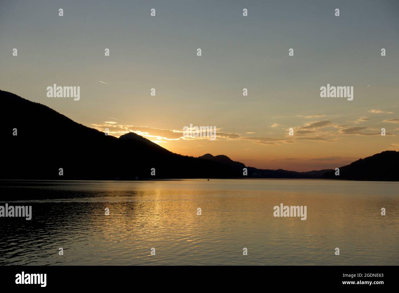 Peace and tranquillity with orange and darkening sky reflected in the calm lake at sunset. Alpine mountain backdrop, Fuschl lake, Austria Stock Photo
