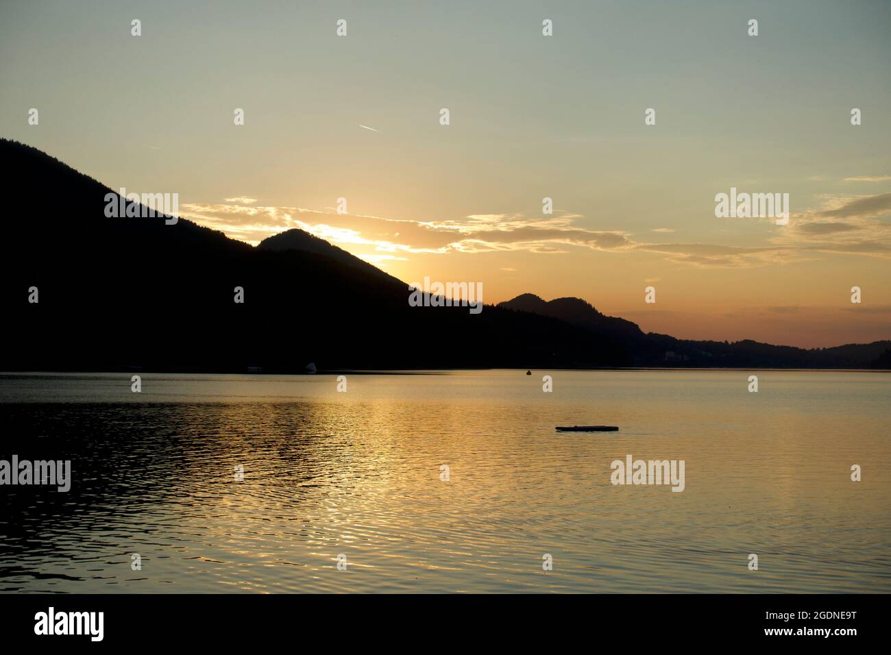 Orange sunset straight horizon against Austrian mountain backdrop with beautiful Alpine lake reflections and paddle board silhouette, Fuschl am See Stock Photo