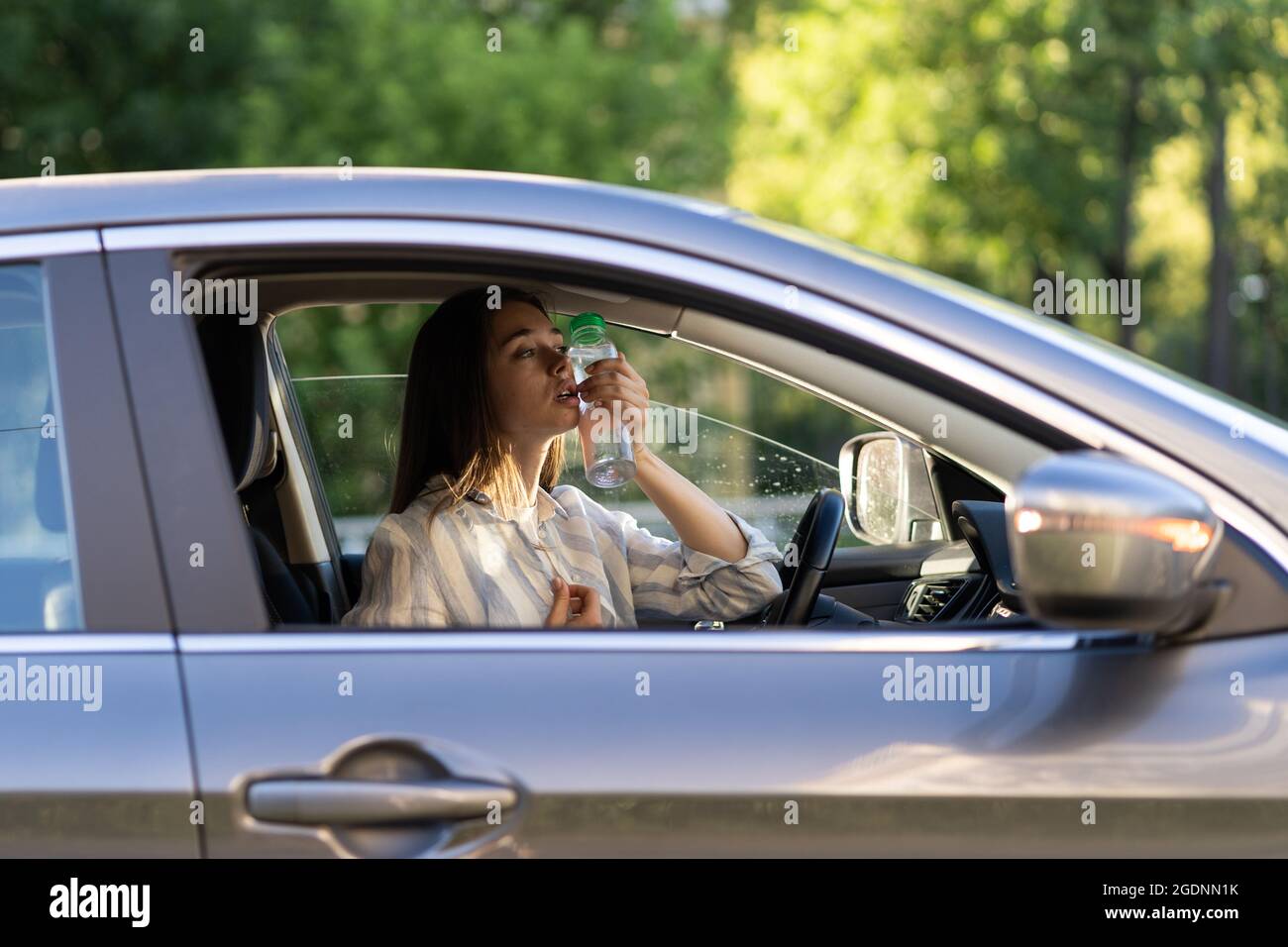 Exhausted girl driver suffering from headache, heat, hot weather applies bottle of water to forehead Stock Photo