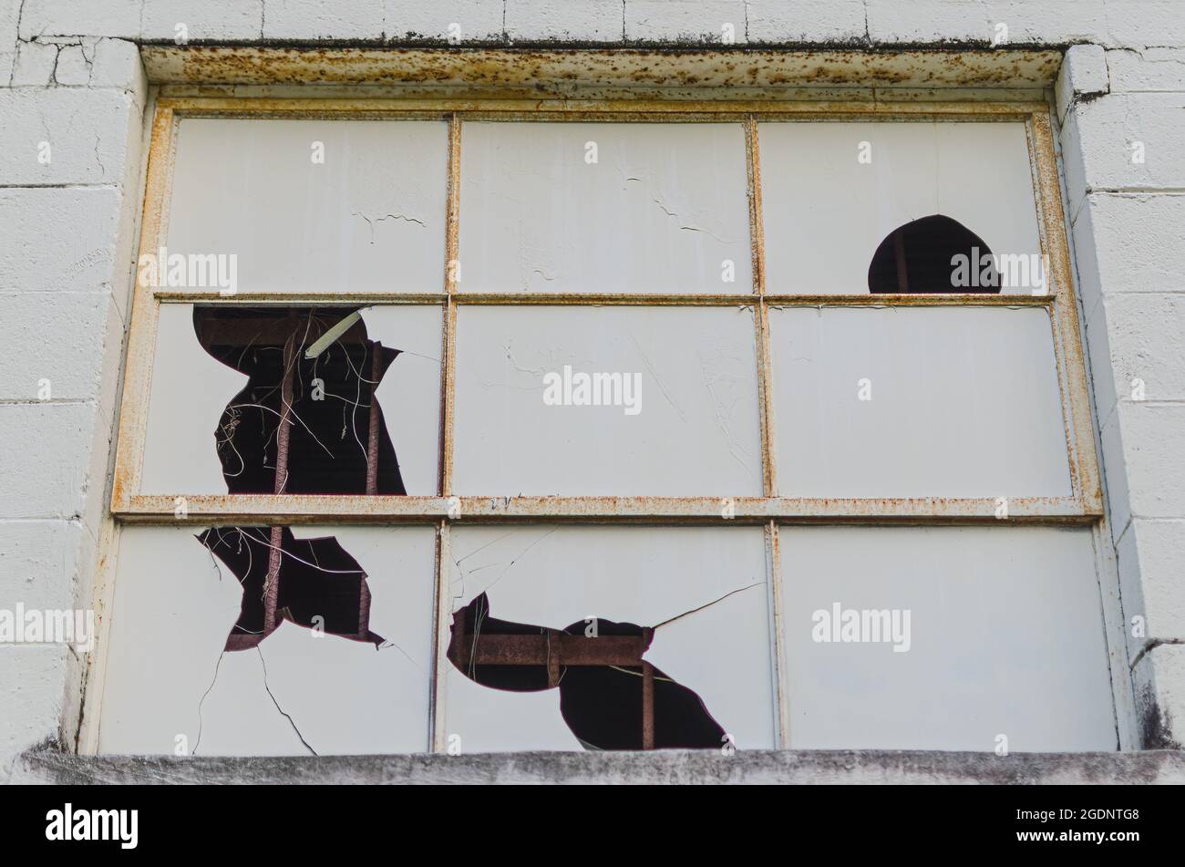 Vacant building with broken window, rusted frame and cracked concrete wall. Stock Photo