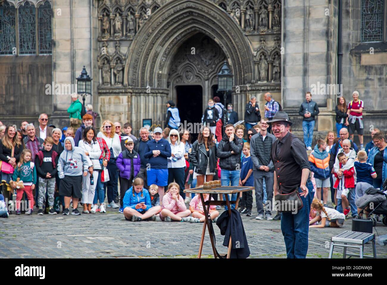 Royal Mile Edinburgh, Scotland, UK. 14th August 2021. Sun came out for the Fringe Festival, 2nd weekend for the scaled back event in the capital city. Crowds arrived but nothing like pre-covid years. Pictured: James James magician and comedian entertains the audience at West Parliamnet Square. Credit: Arch White/Alamy Live News. Stock Photo