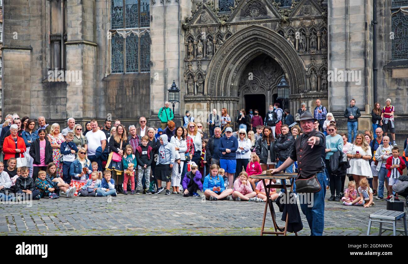 Royal Mile Edinburgh, Scotland, UK. 14th August 2021. Sun came out for the Fringe Festival, 2nd weekend for the scaled back event in the capital city. Crowds arrived but nothing like pre-covid years. Pictured: James James magician and comedian entertains the audience at West Parliamnet Square. Credit: Arch White/Alamy Live News. Stock Photo