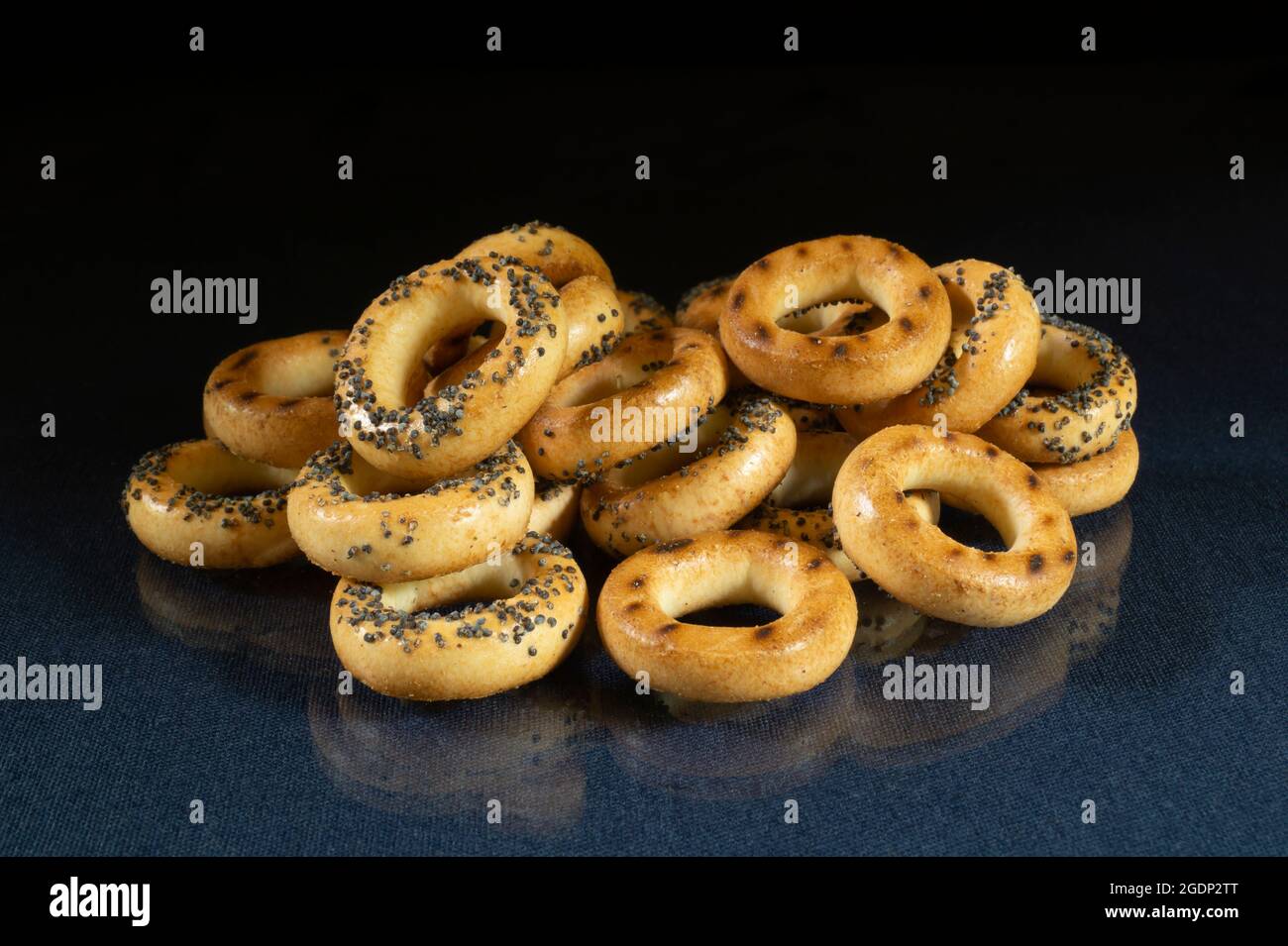Small bagels with a poppy on the table with a reflection. Food products on a black background Stock Photo