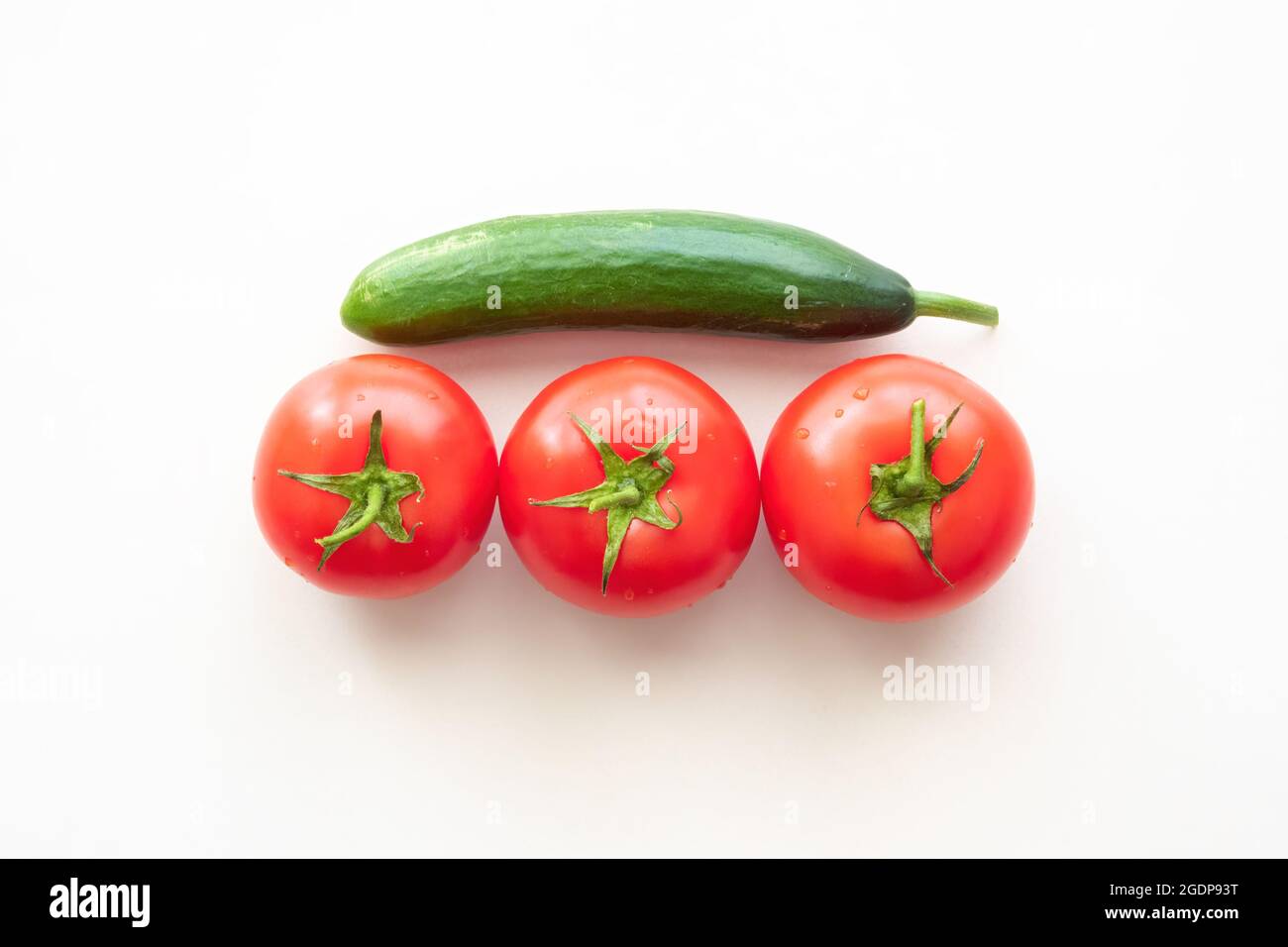 Three red ripe tomatoes with one green cucumber above them Stock Photo ...