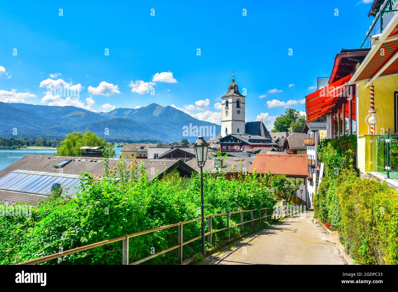 View of St. Wolfgang catholic church in the summer through narrow street in St. Wolfgang im Salzkammergut, Austria. St. Wolfgang is a popular lakeside Stock Photo