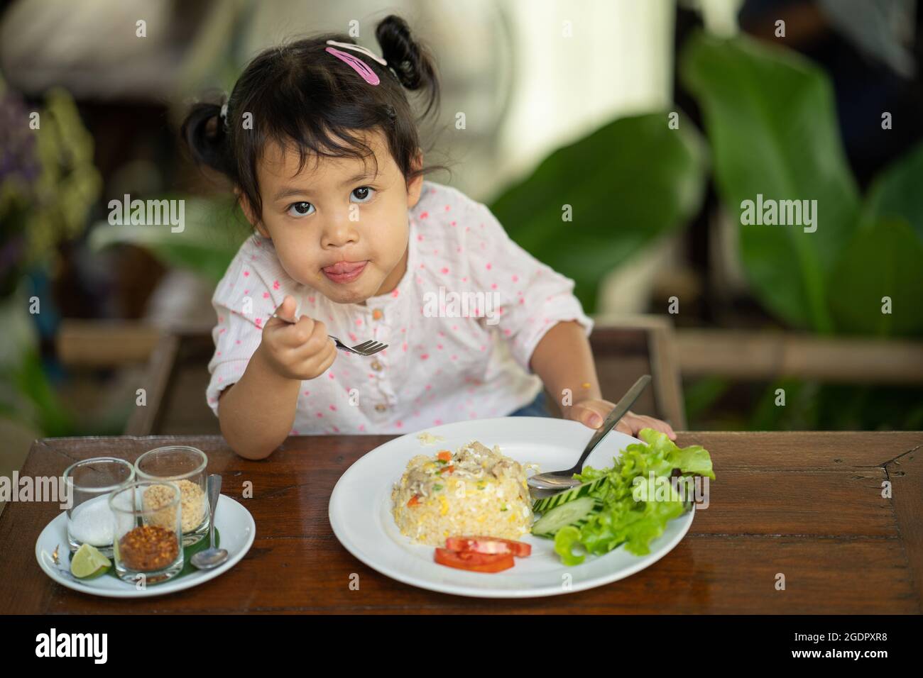 Cute Southeast Asian female child eating breakfast  at a wooden table Stock Photo