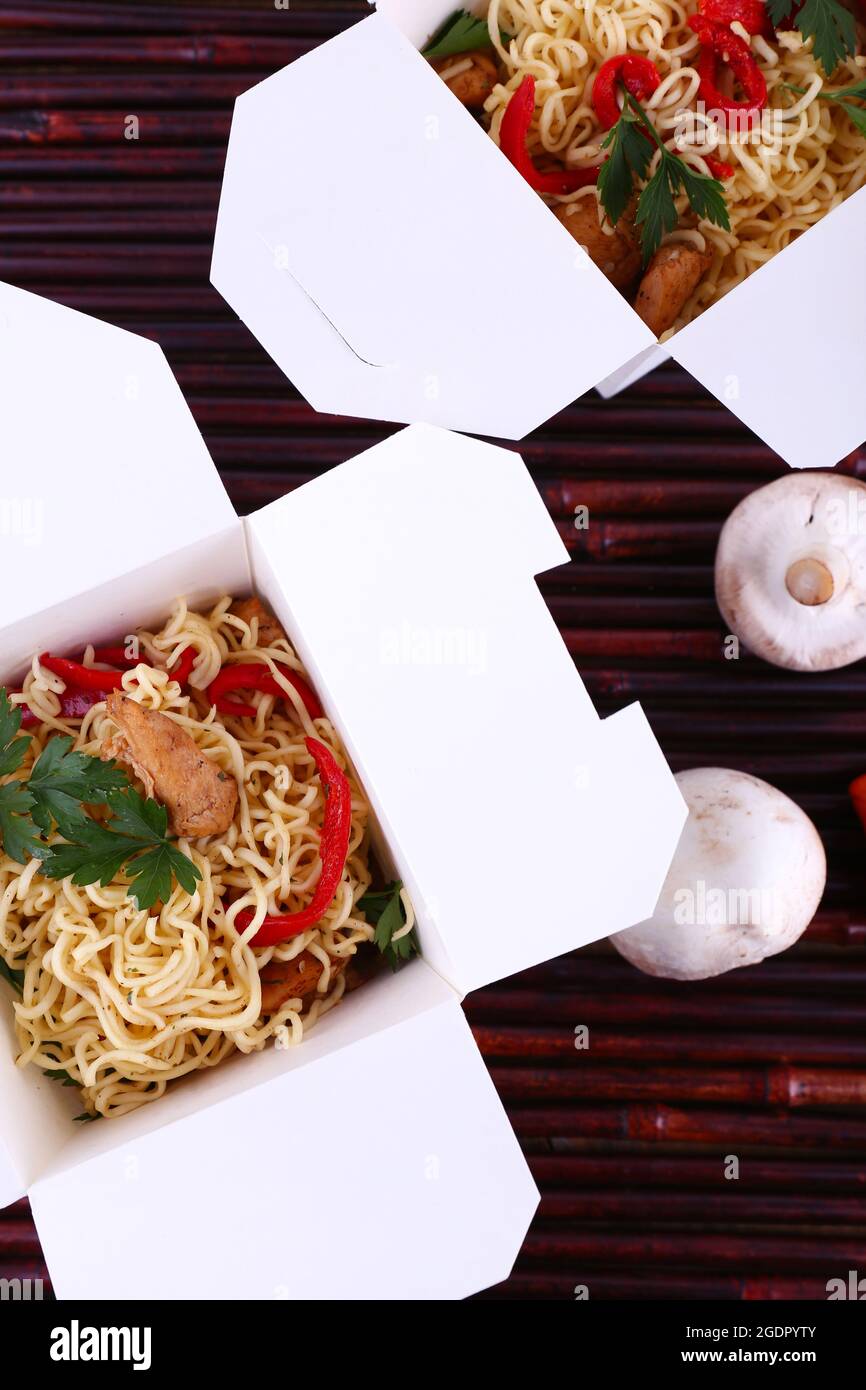Chinese noodles in takeaway boxes on bamboo mat background Stock Photo