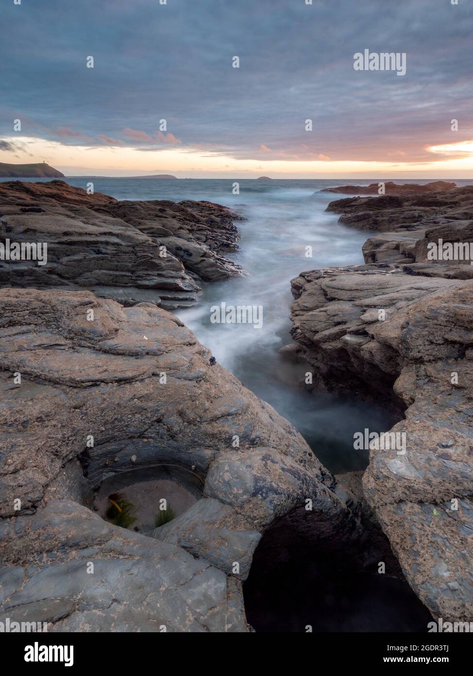 Water streaming into a channel in the slate ledges of the North Cornwall coast at sunset Stock Photo