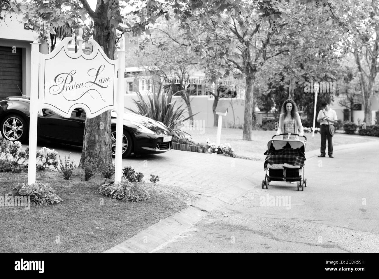 JOHANNESBURG, SOUTH AFRICA - Jan 05, 2021: A female with a pram and a mailman delivering mail in a wealthy suburban neighborhood street Stock Photo