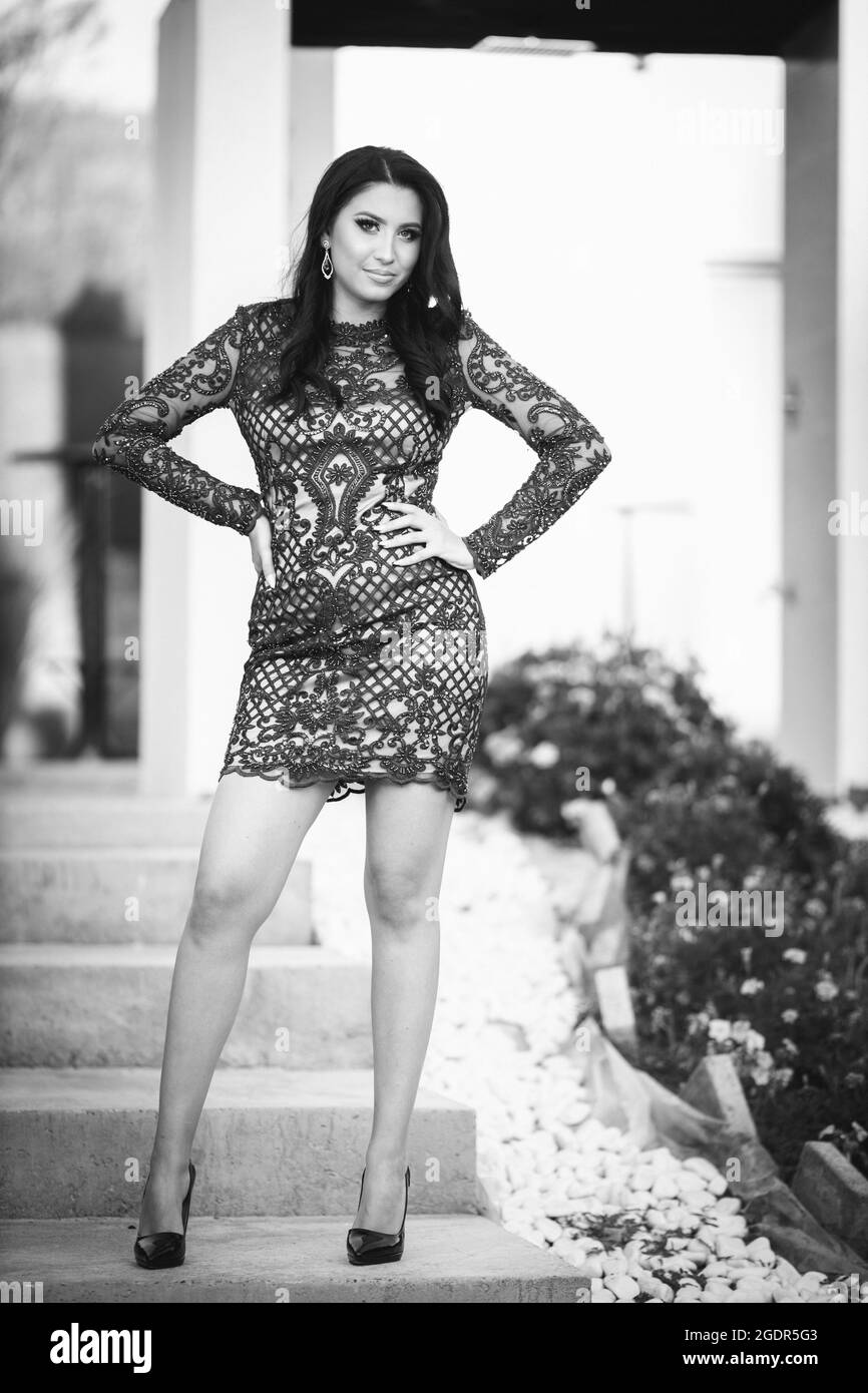 Grayscale shot of a young woman standing on the stairs in a classy dress  Stock Photo - Alamy