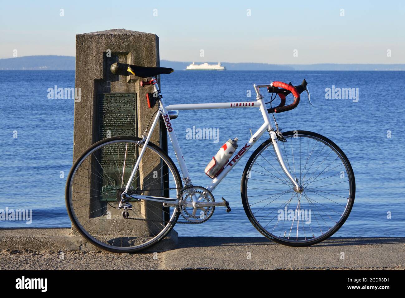 A ferry traverses Puget Sound as a rider takes a hard earned rest stop at Alki Beach Stock Photo