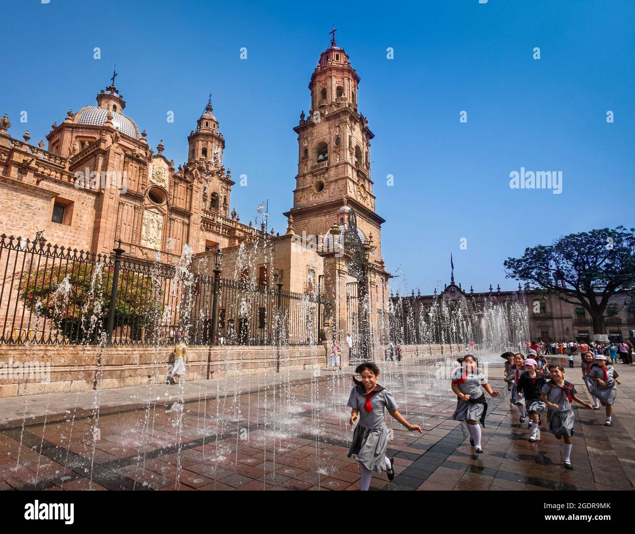 Schoolgirls run through a fountain in the plaza next to the cathedral in Morelia, Michoacan, Mexico. Stock Photo