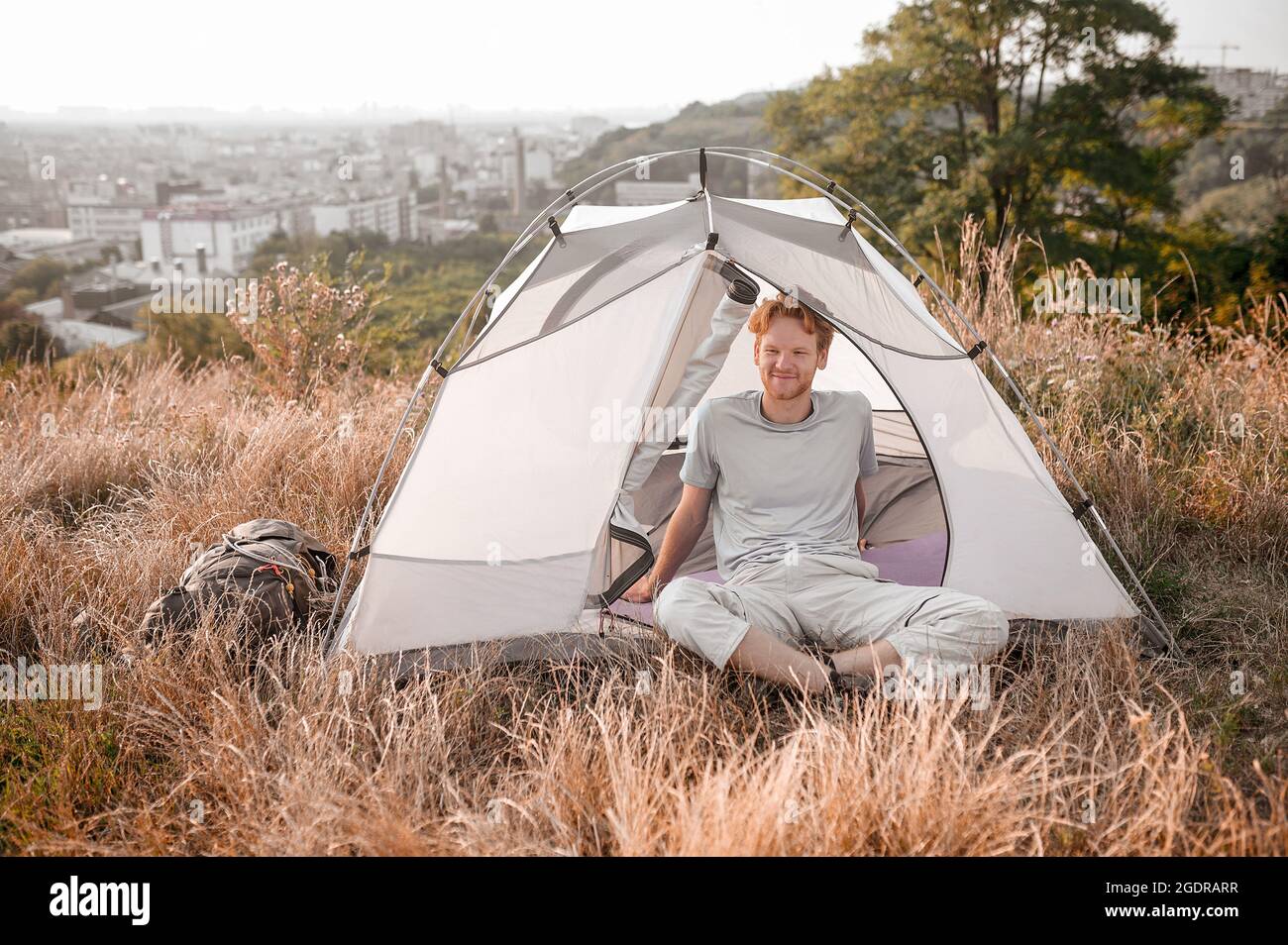 Early morning. A ginger man sitting near the tent and feeling sleepy and relaxed Stock Photo