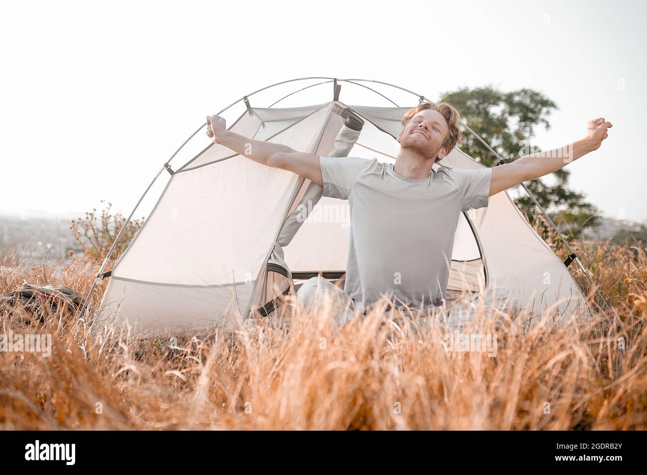 Early morning. A ginger man sitting near the tent and feeling sleepy and relaxed Stock Photo