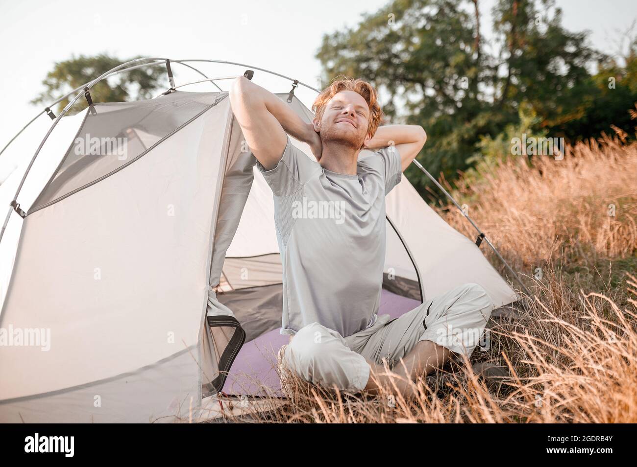 Early morning. A ginger man sitting near the tent and feeling sleepy and relaxed Stock Photo