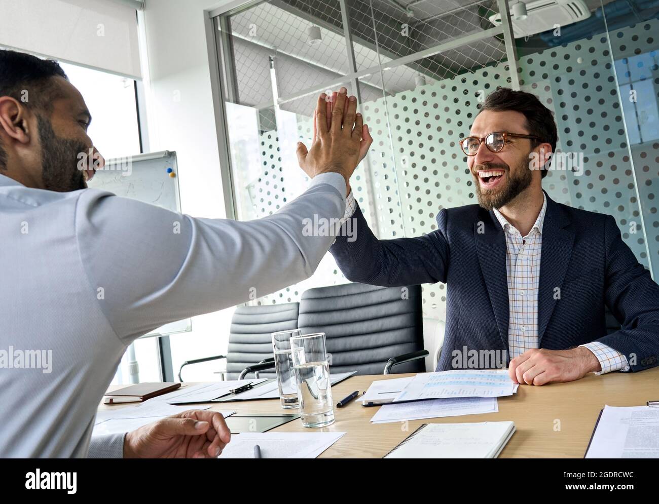 Two happy diverse partners businessmen giving high five at meeting room. Stock Photo