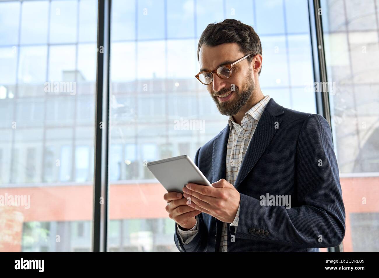 Smiling mature bearded businessman holding tablet device standing in office. Stock Photo