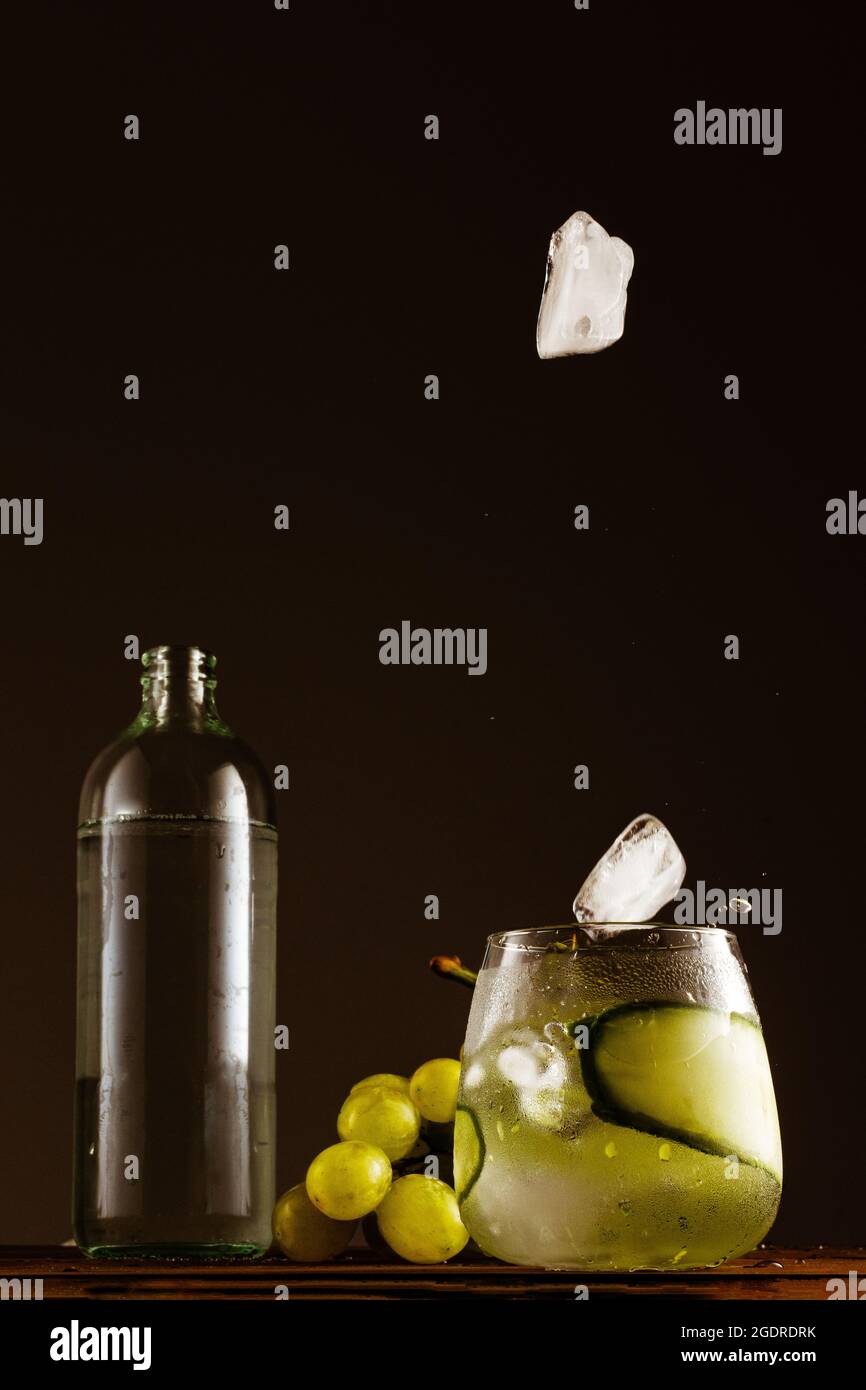 Vertical shot of ice cubes falling into a refreshing drink on a black ...