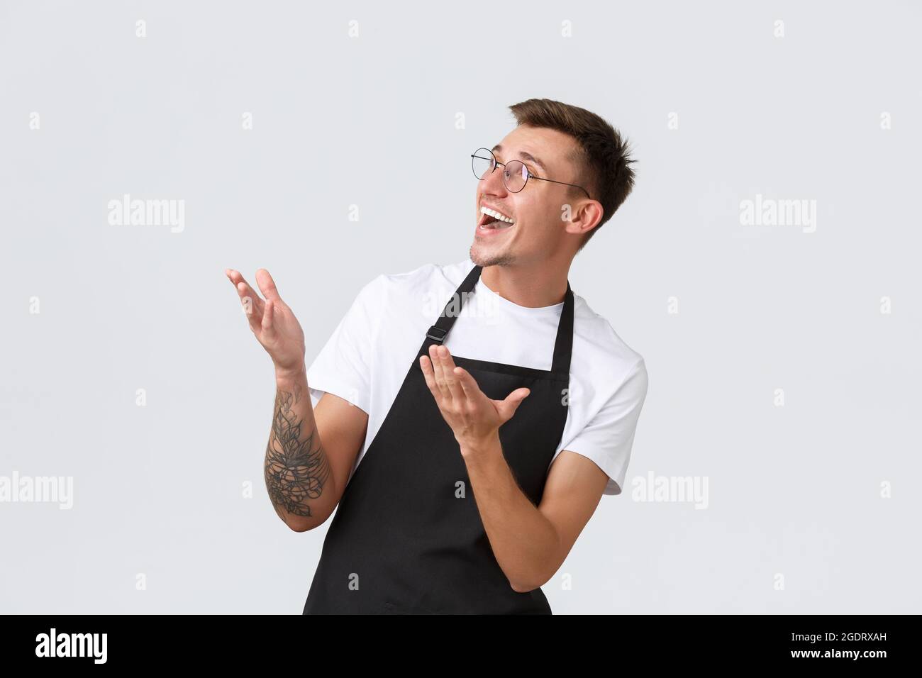 Small retail business owners, cafe and restaurant employees concept. Surprised and happy barista, salesman in black apron and glasses pointing and Stock Photo