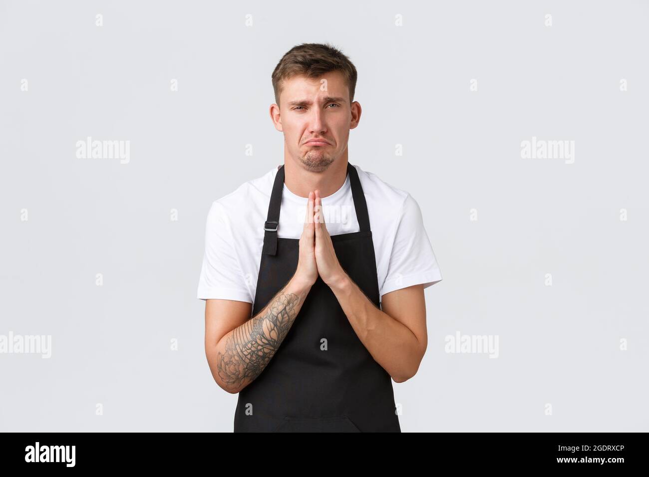 Employees, grocery stores and coffee shop concept. Upset sobbing barista, waiter in black apron begging for day-off, holding hands in pray and pouting Stock Photo