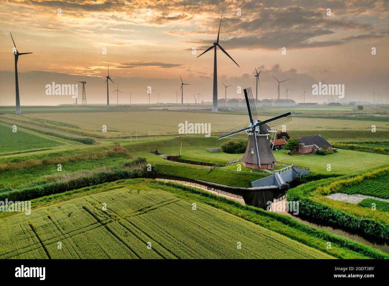 The Netherlands. Eemshaven. Wind park Eemsmond. Wind turbines. Background: ancient windmill (1897) called Goliath. Sunrise. Aerial. Stock Photo