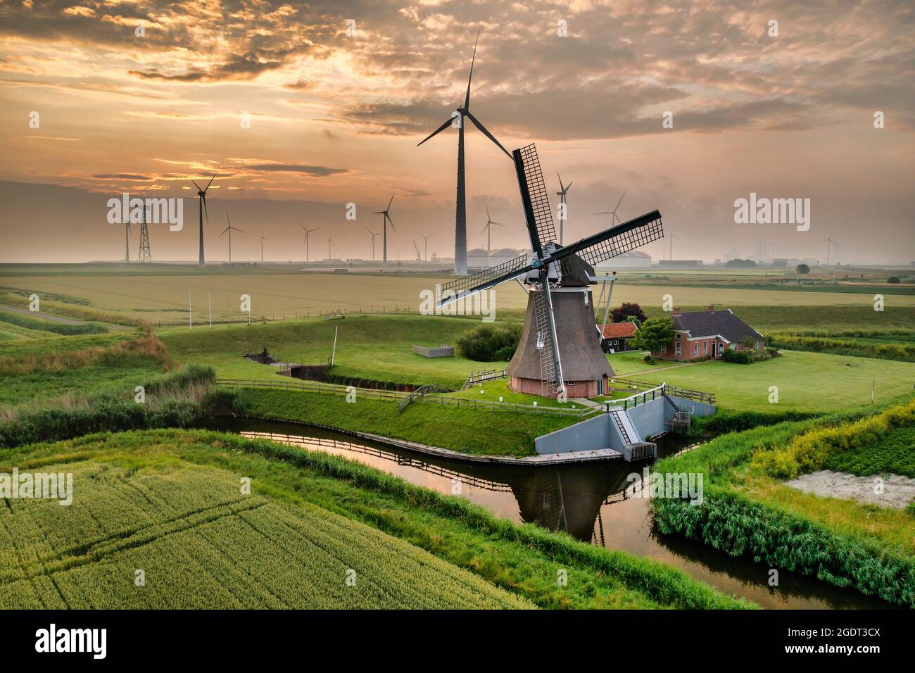 The Netherlands. Eemshaven. Wind park Eemsmond. Wind turbines. Background: ancient windmill (1897) called Goliath. Sunrise. Aerial. Stock Photo