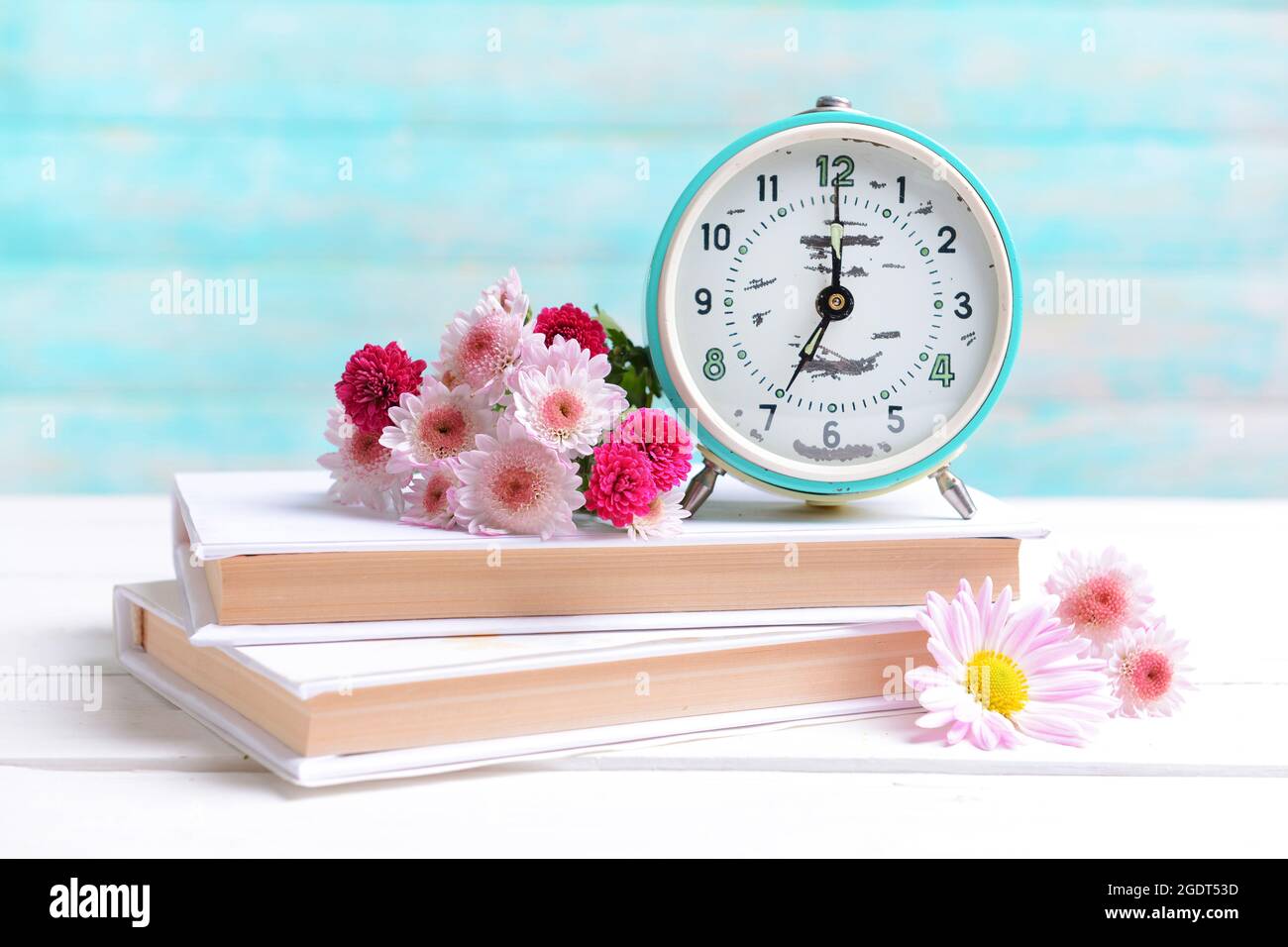 Beautiful flowers with clock and book on table on light blue ...