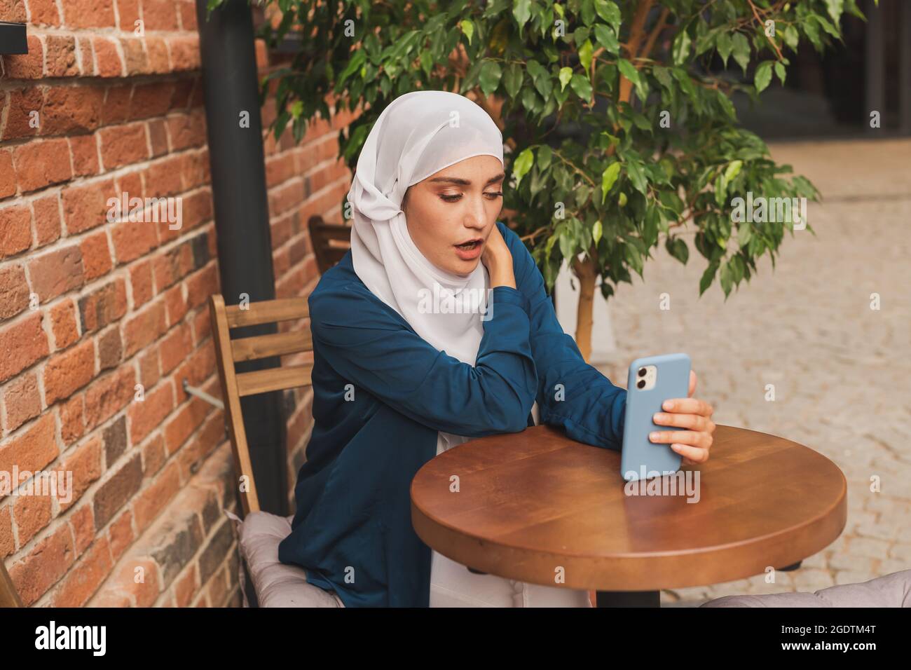 Happy muslim woman having video call on smartphone in outdoor cafe ...