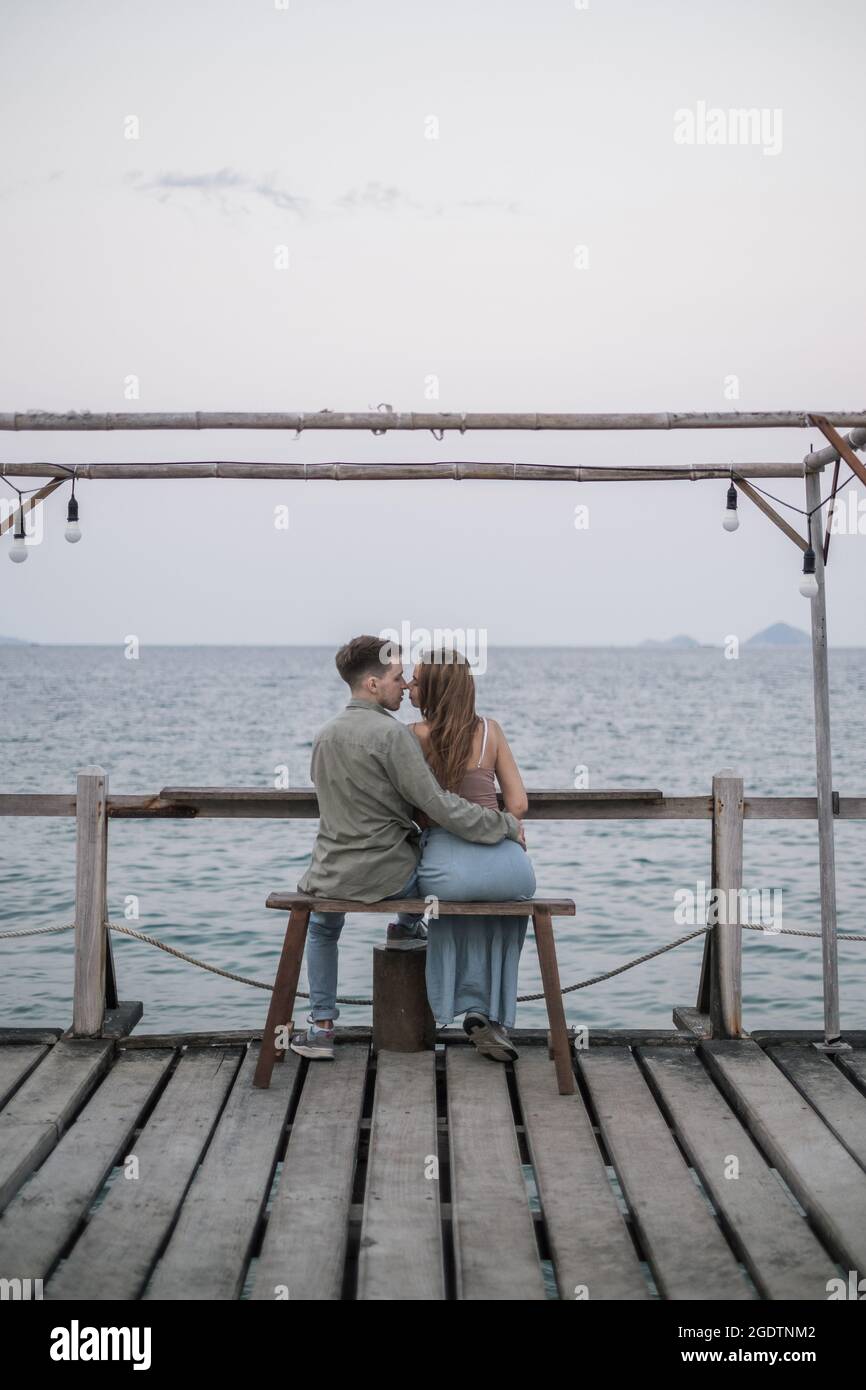 Lovely couple sitting on the wooden bench on the pier. Kissing and Cuddling. Millennials. Romantic picture. High quality photo  Stock Photo