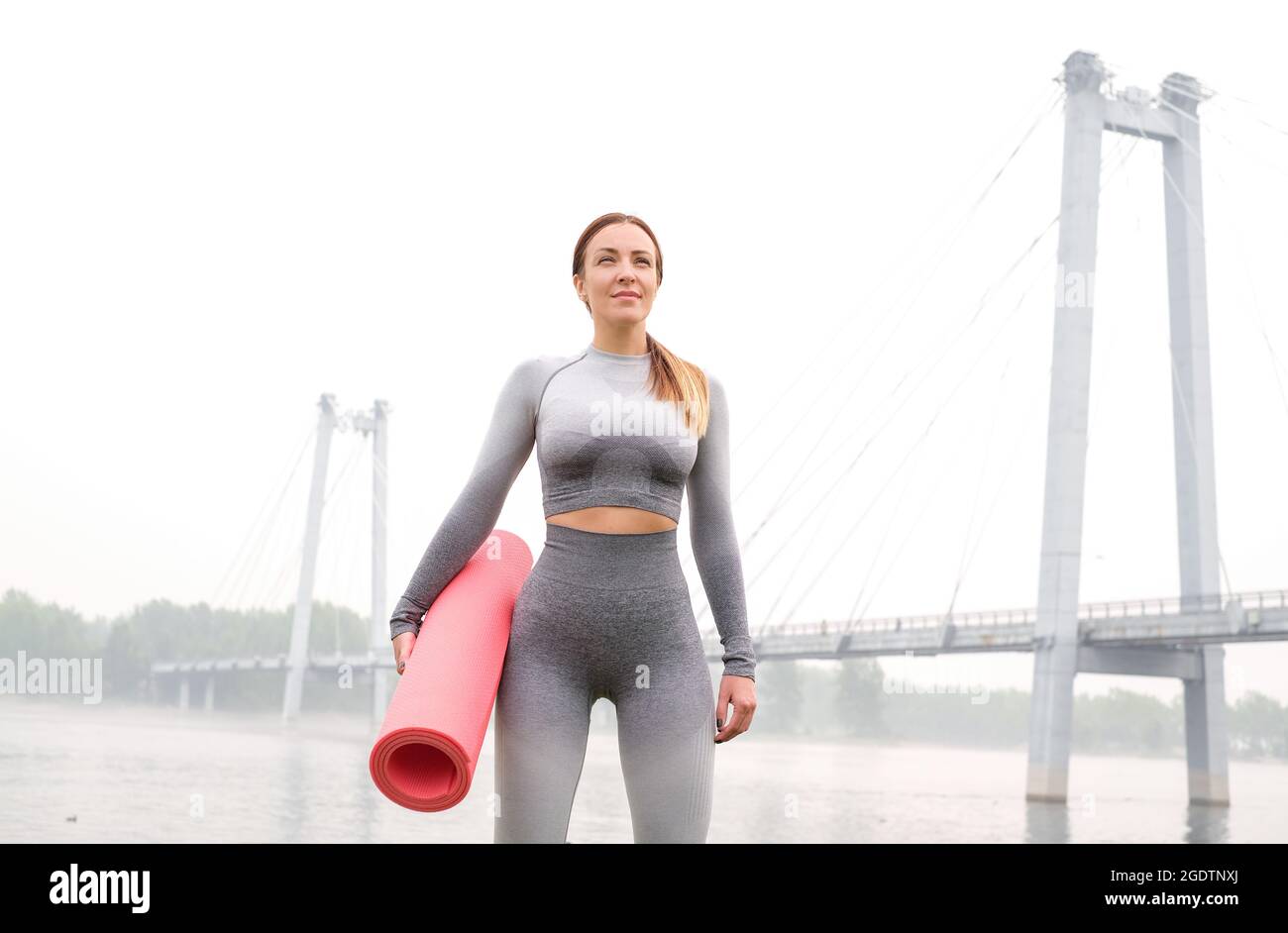 Woman dressed leggings and top with pink mat doing yoga in summer. urban background. Healthy sport lifestyle concept. Active and athletic female exerc Stock Photo