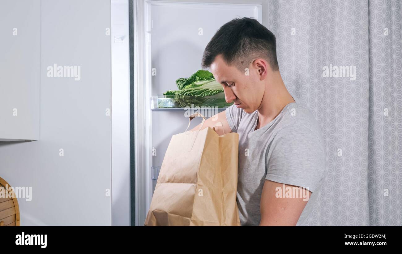 Young man puts different food products into large fridge Stock Photo