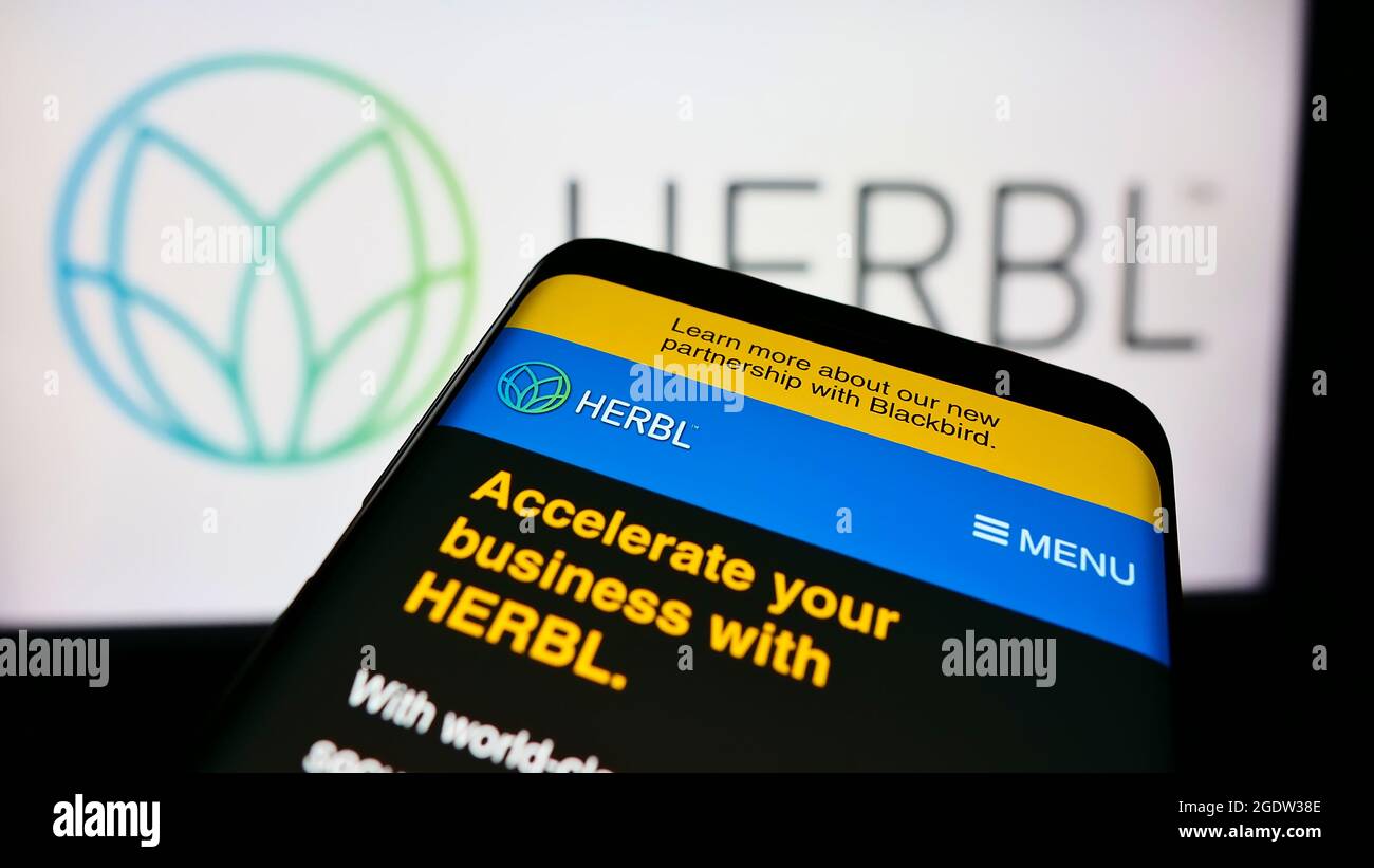 Cellphone with webpage of US cannabis supply chain company HERBL on screen in front of business logo. Focus on top-left of phone display. Stock Photo