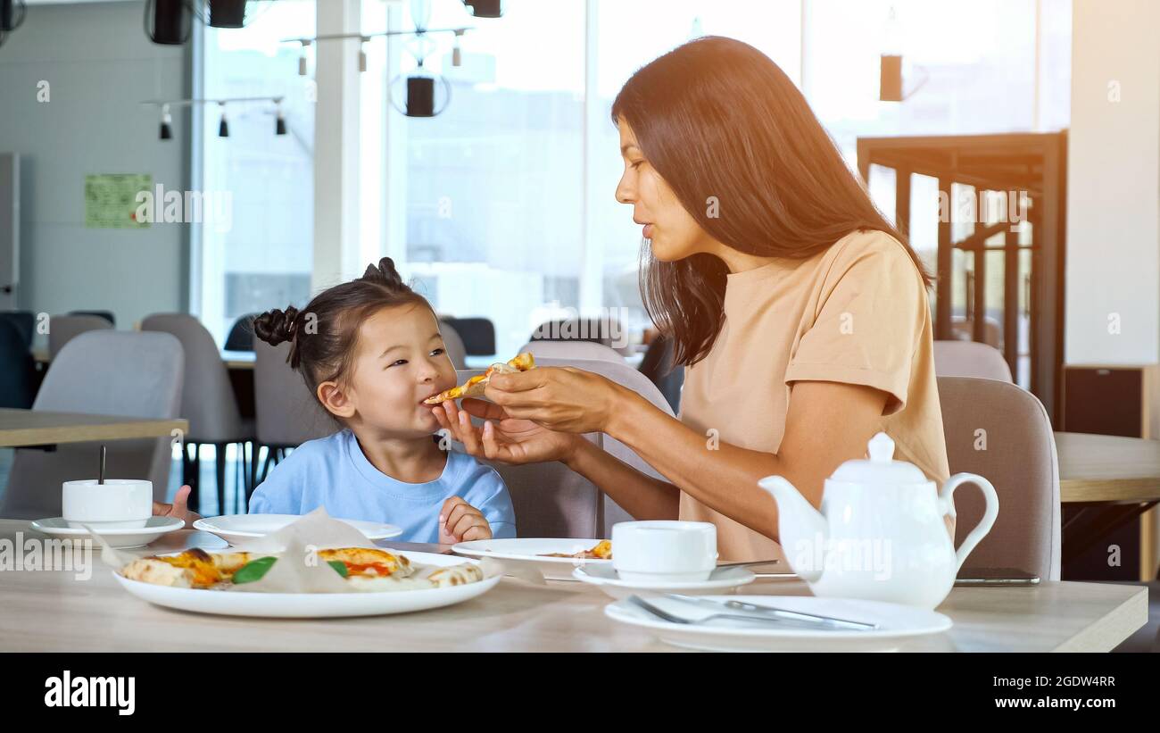 Lady mom holds pizza slice and daughter eats in cafe Stock Photo - Alamy