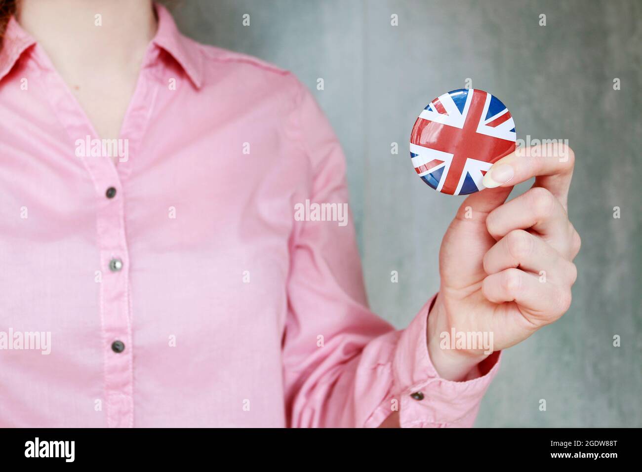 The flag of Great Britain, commonly known as the Union Jack printed on button badge, holding by woman in her beautiful hand. Stock Photo