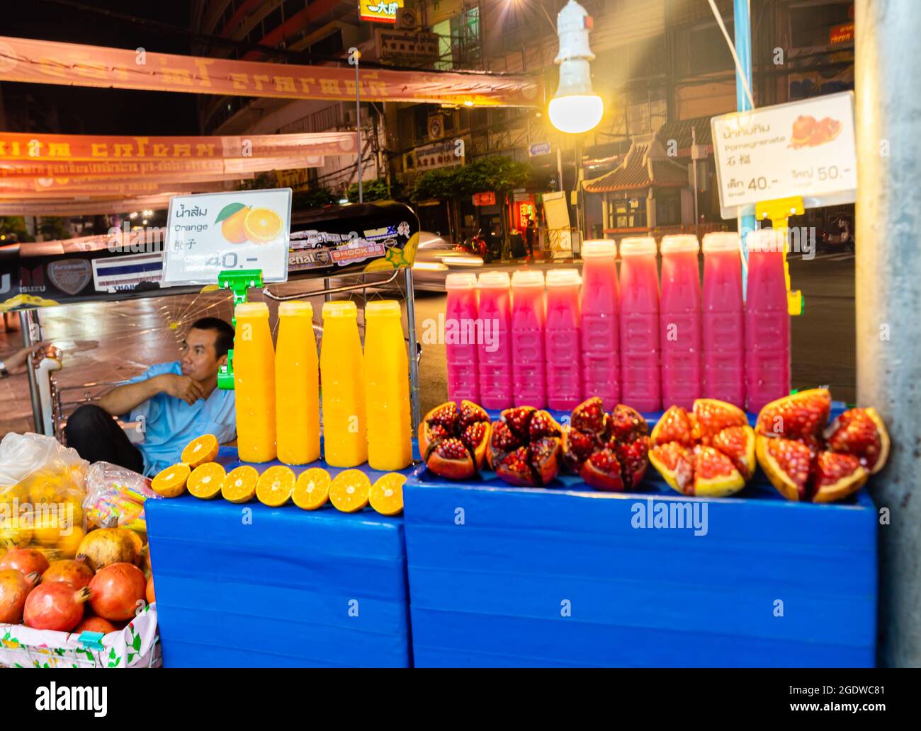 Street vendor selling fruits and juices at the lit up stall, in the night, Yaowarat Rd, Chinatown, Bangkok, Thailand Stock Photo