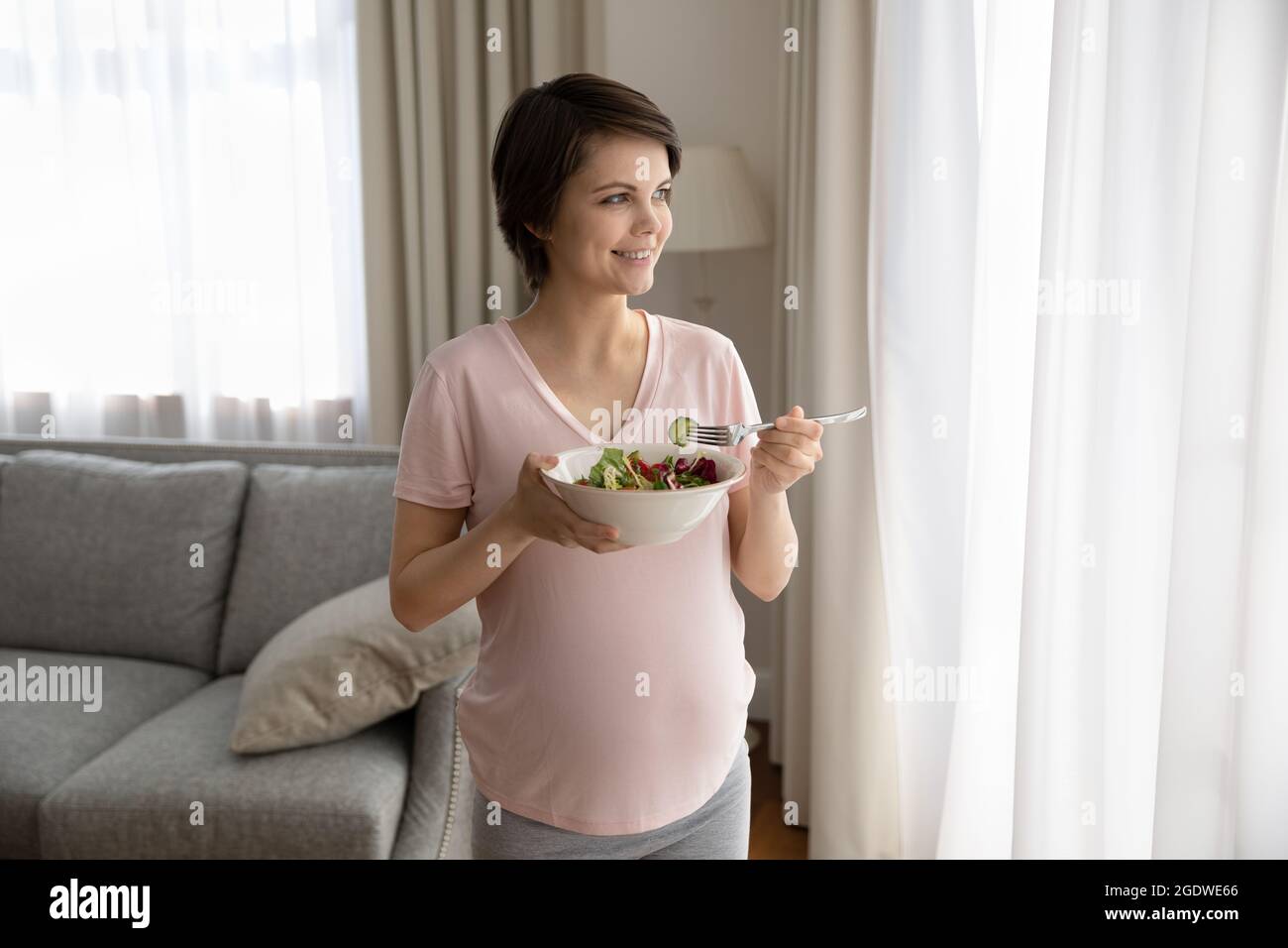 Happy young pregnant woman holding bowl with fresh vegetable salad Stock Photo