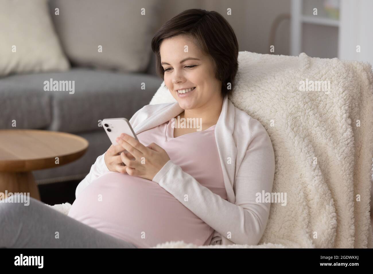 Happy young pregnant woman enjoying leisure at home, using smartphone Stock Photo