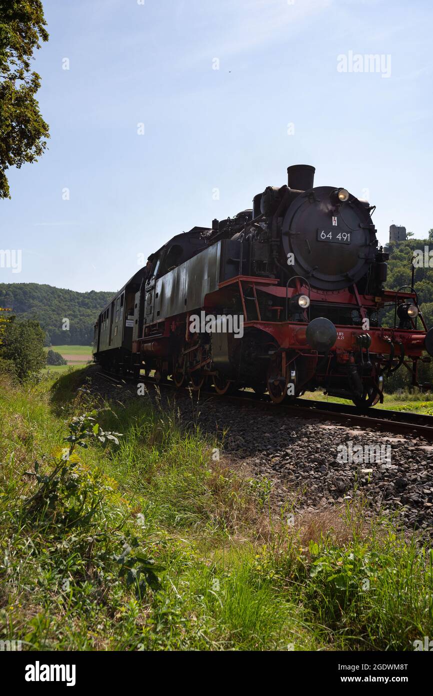 Streitberg, Germany. 15th Aug, 2021. A historic steam locomotive passes Streitberg in Franconian Switzerland. The locomotive is a passenger train tender with the number 64 491 that was built in 1940 by the manufacturer 'Orenstein & Koppel' in Berlin. According to the homepage of the 'Dampfbahn Fränkische Schweiz e.V.', the locomotive was taken out of service in Crailsheim in 1974 as one of the last of its class at the Deutsche Bahn (DB) and was also used for film productions such as 'Unsere Mütter, unsere Väter'. Credit: Nicolas Armer/dpa/Alamy Live News Stock Photo