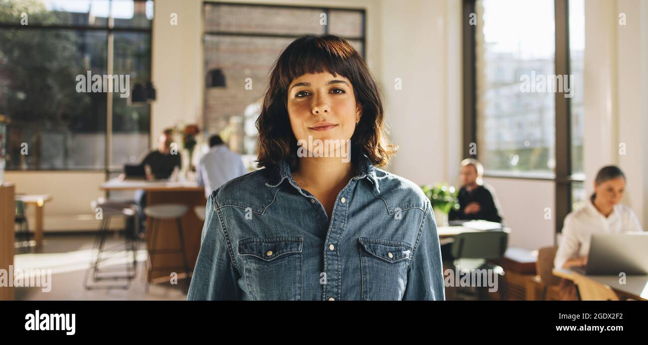 Portrait of freelancer standing in co-working space. Confident businesswoman looking at camera. Stock Photo