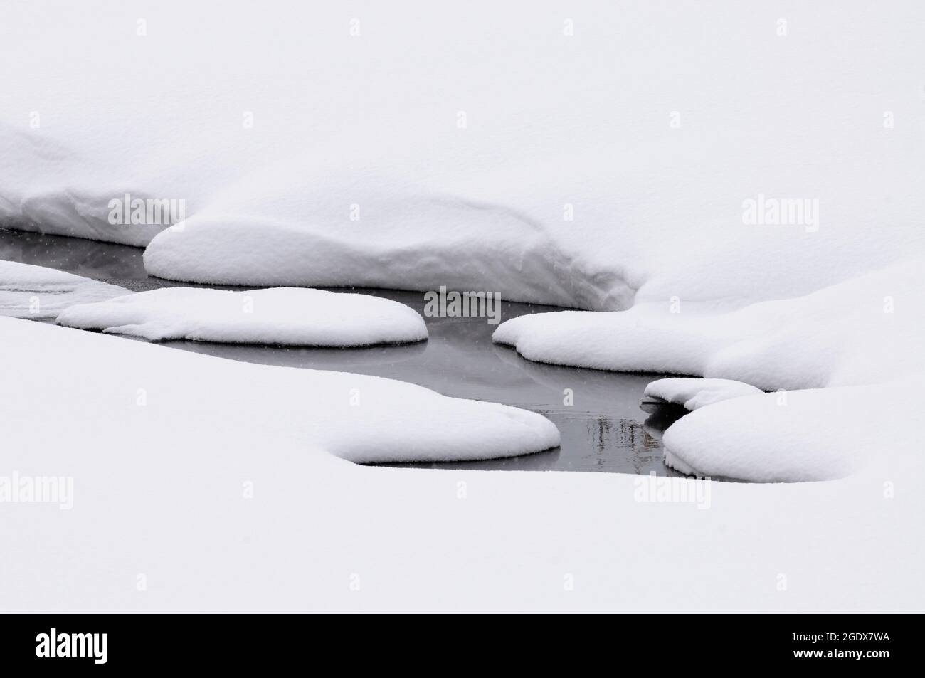 Small stream with open water in thick snow Stock Photo